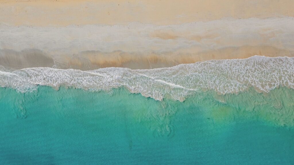 Turquoise ocean waves gently crash on a sandy beach.