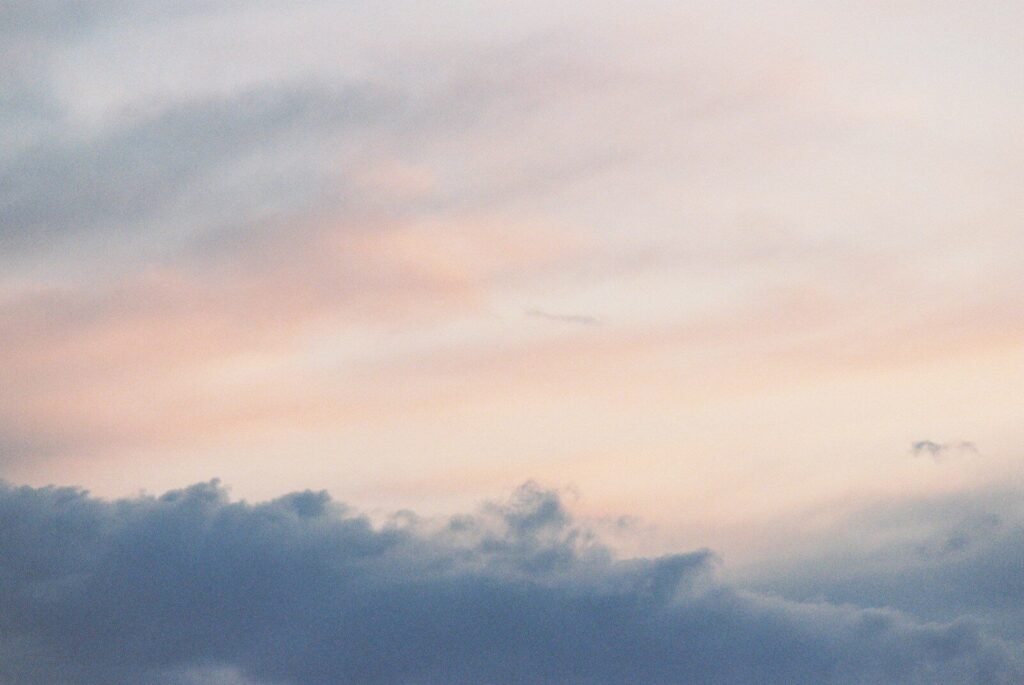 Soft pink and grey clouds drifting across a pale sky