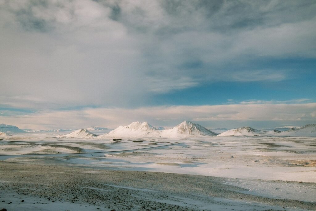 A long road winding through a vast snow covered landscape with distant mountains