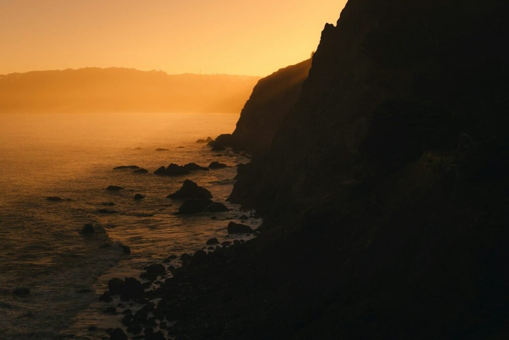 A rocky coastline in silhouette against a warm orange sky at low sun